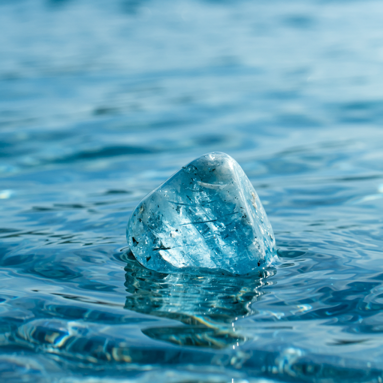 Gema azul aguamarina preciosa translúcida, pulida y brillante, emergiendo de la superficie de agua azul clara.