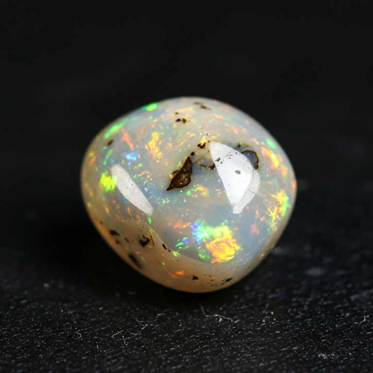 Cabujón de ópalo blanco con fuego Ópalo cabujón blanco lechoso pulido, mostrando un juego de color intenso con destellos verdes, naranjas y rojos.